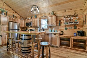 Cocina de madera rústica con barra, taburetes de madera y un gran barril como elemento central.