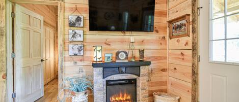 Una habitación acogedora con chimenea, paredes de madera, televisor montado y fotografías enmarcadas.