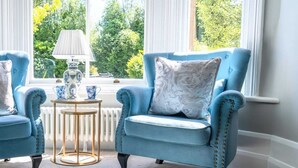 A room with two blue armchairs, a small round table with a lamp, and a view of greenery outside. - Boutique Family Home, Garden, Parking 3 cars, 2 Living Rooms. Cornwall (Wadebridge)
