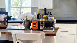 A kitchen with white cabinets, a wooden countertop, a vase with white flowers, a box of Cornish Tea, a Nescafé Gold Blend coffee jar, and a basket with kitchen utensils. - Boutique Family Home, Garden, Parking 3 cars, 2 Living Rooms. Cornwall (Wadebridge)