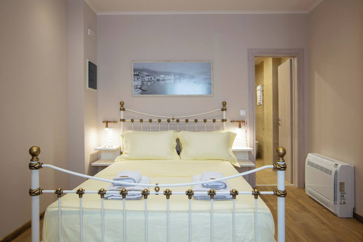 A neatly made bed with a white and gold frame, a bedside table with a lamp, and a wall-mounted picture.
