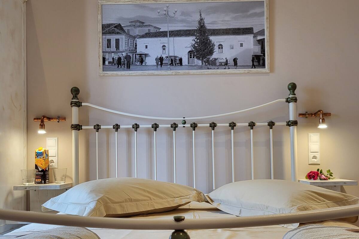 A neatly made bed with a metal frame, a bedside table with a lamp, and a framed picture on the wall.