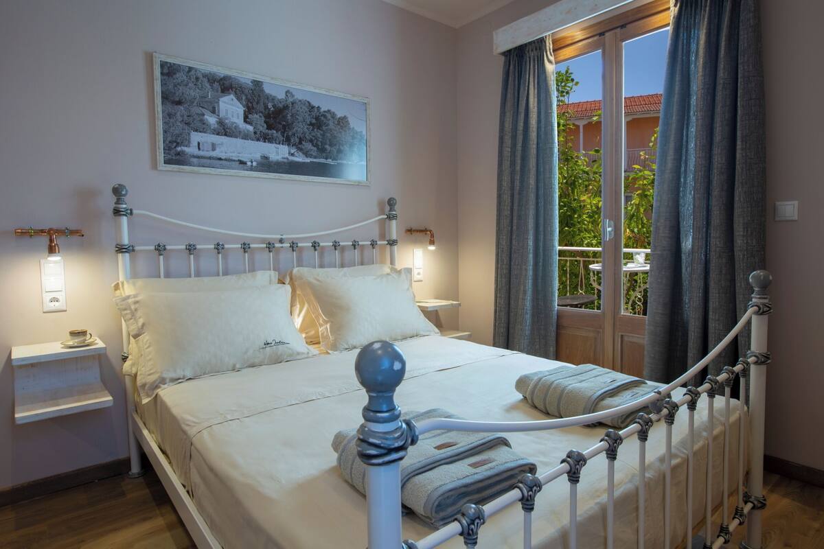 A neatly made bed with white linens and a metal headboard, a bedside table with a lamp, and a window with curtains.