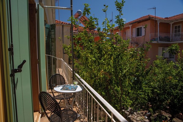 Varanda com mesa e cadeiras, vista para um jardim e edifícios vizinhos.