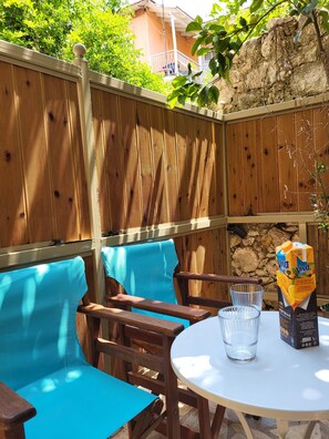 A wooden fence, a table with a box of orange juice, and a chair with a blue cushion. - Bella Vita Boutique Hotel Lefkada (Lefkada)