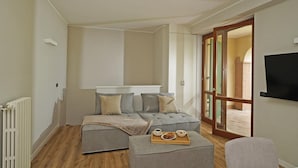 A modern bedroom with a grey sofa bed, a small bedside table with a tray of breakfast, and a TV mounted on the wall. - Casa Monte Cicogna PT 1 by Wonderful Italy (Moniga del Garda)