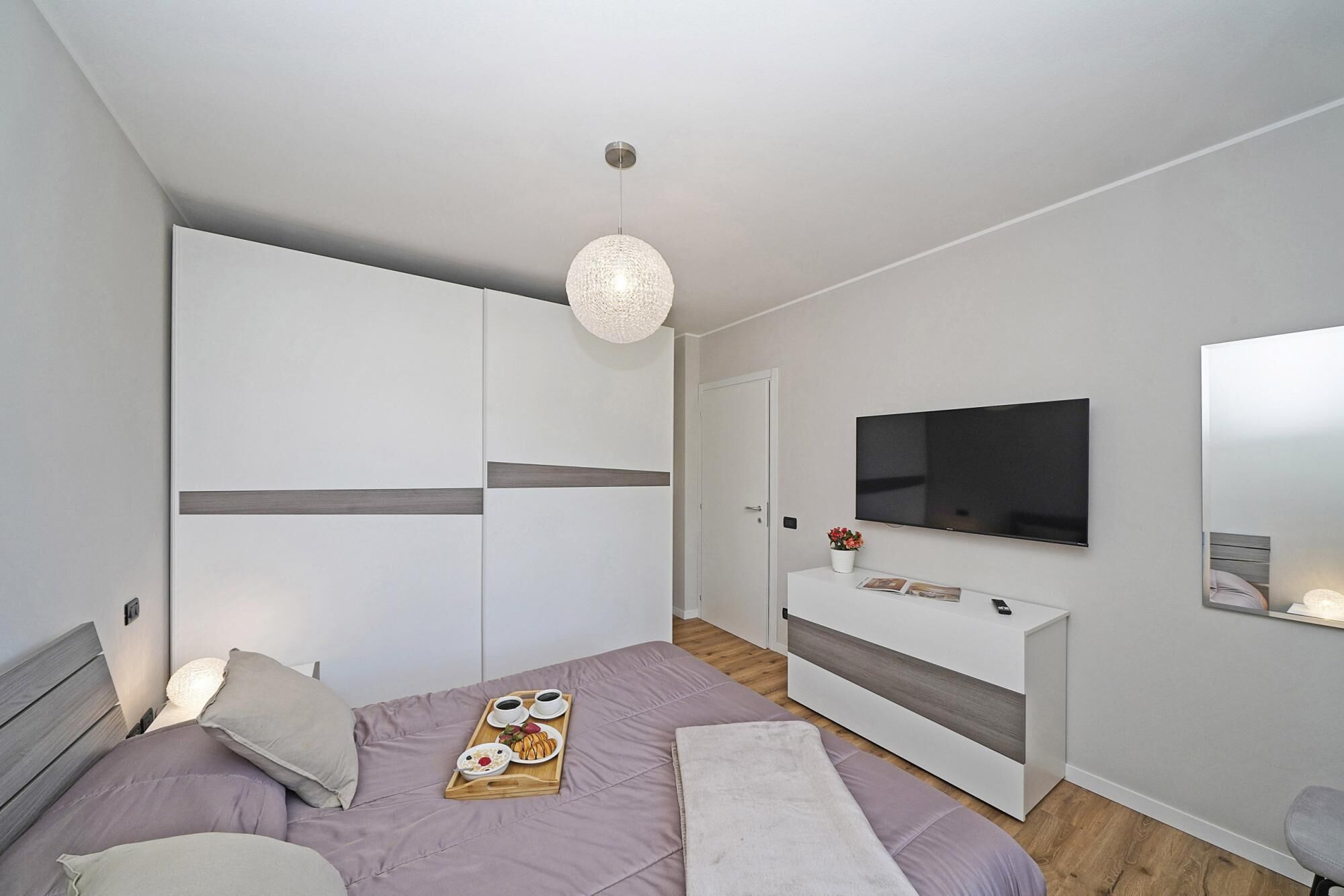 A modern bedroom with a bed, bedside table, TV, wardrobe, and a hanging light fixture.