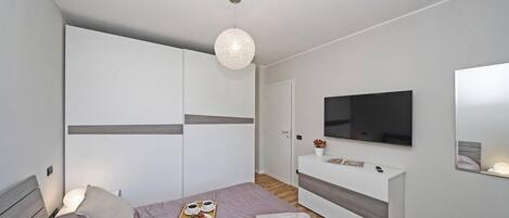 A modern bedroom with a bed, bedside table, TV, wardrobe, and a hanging light fixture.