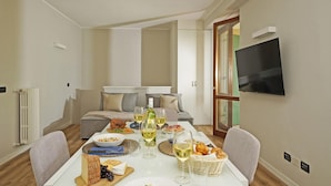 A dining area with a table set for a meal, a sofa in the background, and a TV mounted on the wall. - Casa Monte Cicogna PT 1 by Wonderful Italy (Moniga del Garda)