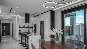 Una cocina moderna con una isla de mármol, electrodomésticos de acero inoxidable y un comedor con mesa de madera y sillas tapizadas en gris.