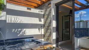 Un área de spa moderna al aire libre con una bañera de hidromasaje, una terraza de madera y una pared de piedra.