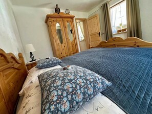 Een slaapkamer met een groot bed, twee kussens, een houten garderobe en een raam met gordijnen.
