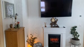 A living room with a fireplace, a mounted TV, and decorative items including a clock and figurines. - Alpine Holiday Home in Lungau (Vordermuhr)
