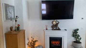 Ein Wohnzimmer mit Kamin, einem an der Wand montierten Fernseher und dekorativen Elementen, darunter eine Uhr und Figuren.