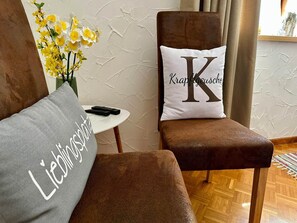 A room with a brown armchair, a grey pillow with 'Lieblingsplatte' text, and a white pillow with 'Krappgeusche' text. - Alpine Holiday Home in Lungau (Vordermuhr)