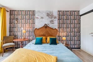 Quarto com uma cama grande, duas mesas de cabeceira, uma cadeira e uma estante.