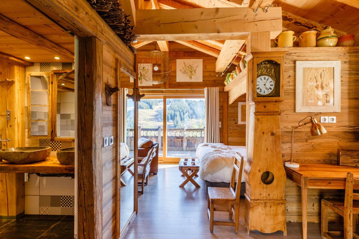 Interior de cabana de madeira com cama acolhedora, área de jantar e vista através de uma porta de vidro.