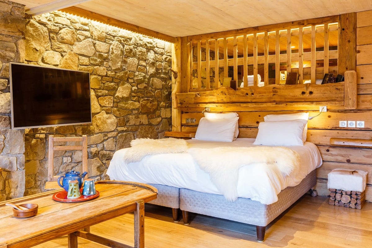 Um quarto acolhedor com parede de pedra, cabeceira de madeira e televisão de tela plana.
