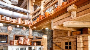 A rustic cabin interior with a stone wall, wooden staircase, and copper cookware displayed on shelves.