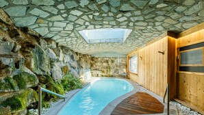A stone-walled indoor pool with a wooden deck and a stone ceiling.