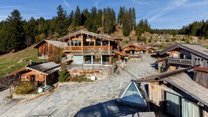 A wooden lodge with a stone courtyard, wooden cabins, and a mountain backdrop.