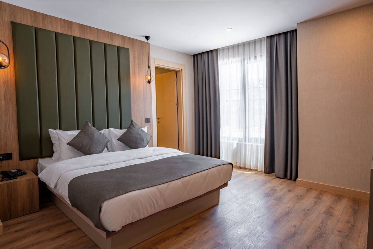 Une chambre d’hôtel moderne avec un grand lit, une tête de lit en bois et une table de chevet avec un téléphone.
