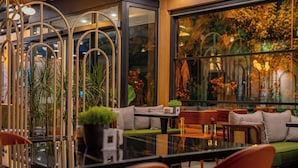 A modern indoor seating area with a glass table, cushioned seating, and potted plants. - Perast City Hotel (Konyaalti)