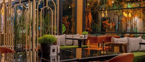 Un área de estar interior moderna con una mesa de vidrio, asientos acolchados y plantas en macetas.