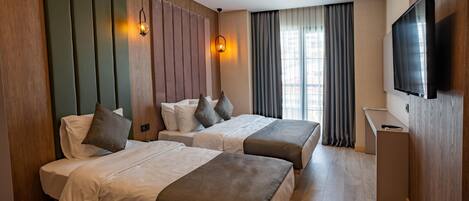Quarto de hotel com duas camas, televisão, escrivaninha e janela com cortinas.