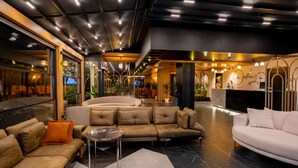 A modern lobby with sofas, a reception desk, and a large window overlooking the street. - Perast City Hotel (Konyaalti)