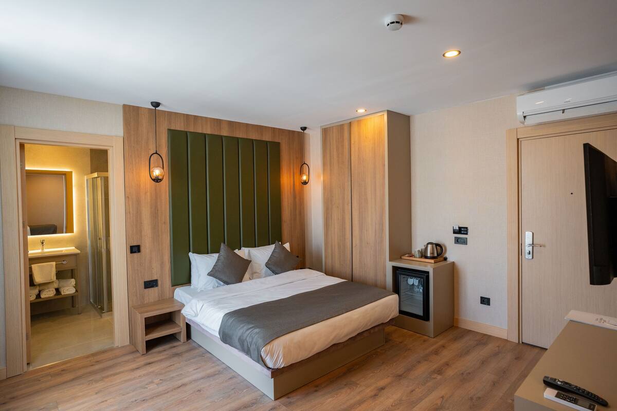 Une chambre d’hôtel moderne avec un lit en bois, une table de chevet avec une bouilloire, un téléviseur intégré et un dressing.