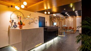 Een hotel receptie met een marmeren balie, een receptiemedewerker en een zithoek met stoelen.