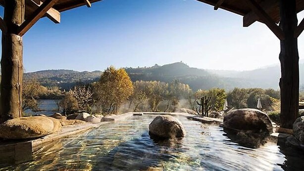 A clear view of a hot spring area with rocks in the water, surrounded by trees and hills in the background.