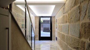 A hallway with stone walls, a glass railing, and a black door with a metal gate.