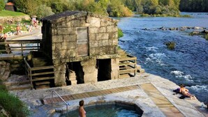 A stone building with a pool and wooden deck by a river.