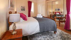 A bedroom with a bed, a nightstand, a lamp, a mirror, and a window with red curtains. - Holly Leaf Cottage - Drum Castle Estate (Banchory)