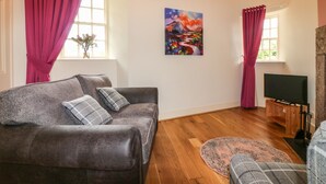 A living room with a grey sofa, a television, and a painting on the wall. - Holly Leaf Cottage - Drum Castle Estate (Banchory)