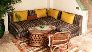 A corner living room with a sofa, patterned cushions, a coffee table, and a large potted plant. - Riad Lalla Mimouna (Marrakech)