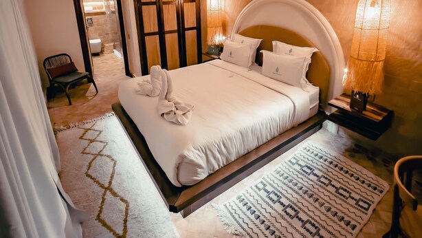 A spacious bedroom with a large bed, a sitting area with a chair, and a bathroom visible through an arched doorway. - Riad Lalla Mimouna (Marrakech)