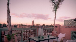 A terrace with a table and chairs, overlooking a cityscape with a prominent tower. - Riad Lalla Mimouna (Marrakech)