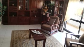 A living room with a wooden cabinet, a brown armchair, a small table, and a patterned rug. - T3 Vivenda Bemposta / Portimão (Portimão)
