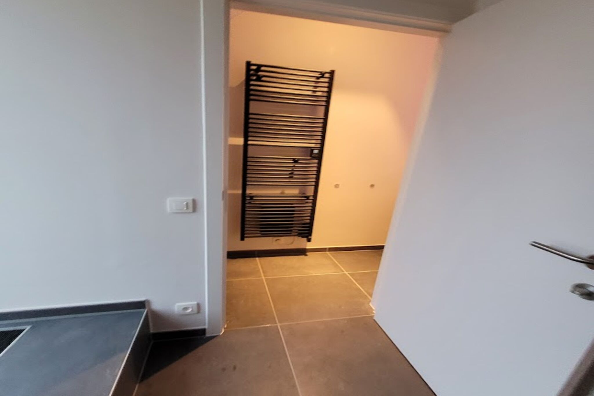 A narrow hallway with a black metal rack against the wall and a door on the right.
