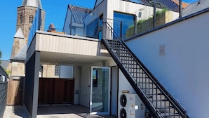 A modern building with a staircase leading to a balcony, a large window, and a visible air conditioning unit.