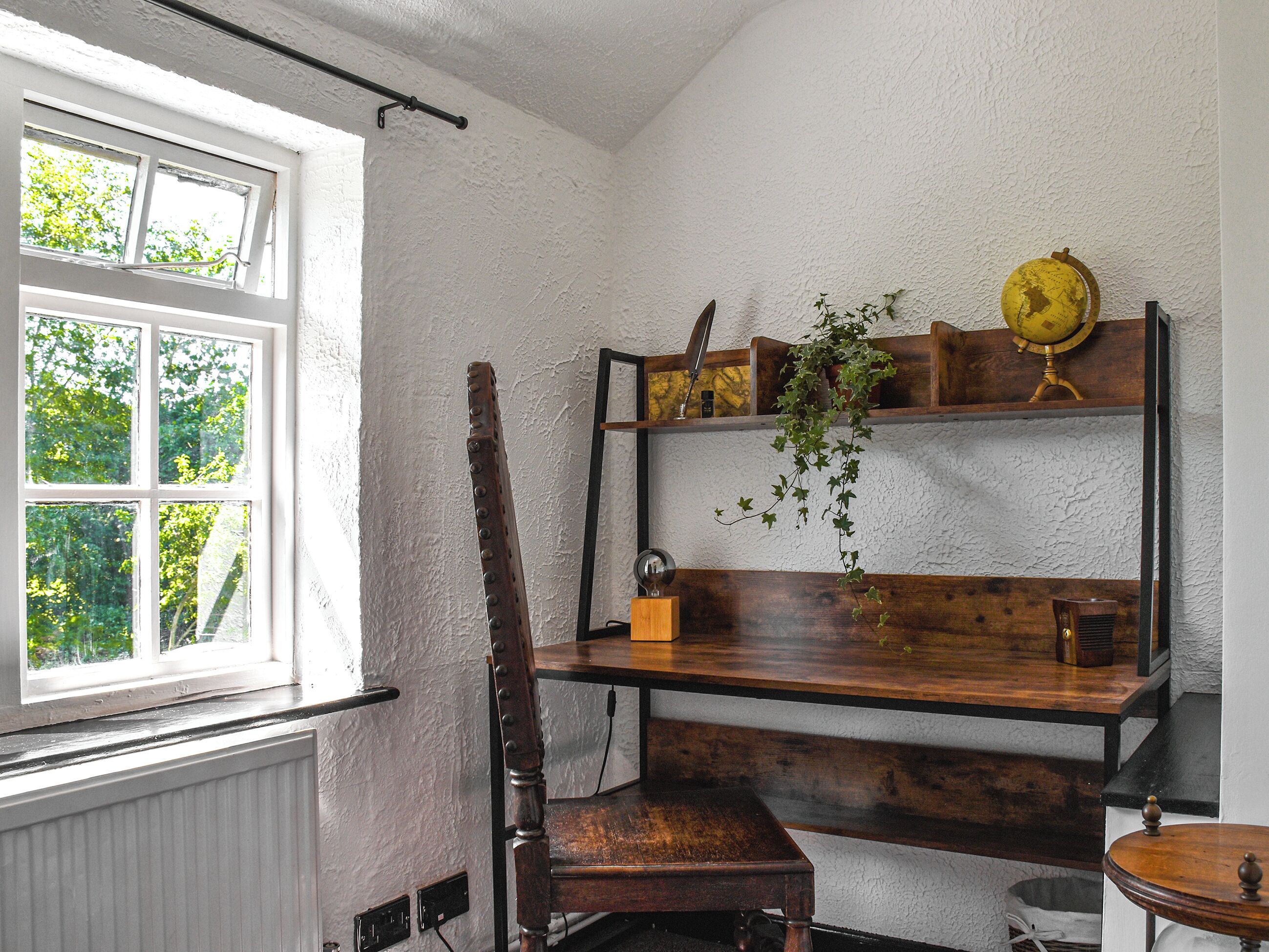 A room with a wooden chair, a wooden table, a shelf with a globe, and a window with a view of trees.