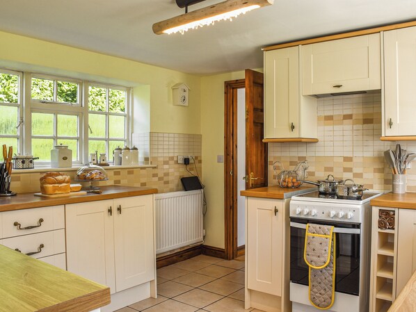 A kitchen with white cabinets, a wooden countertop, a stove, and a window with greenery outside. - 3 bedroom accommodation in Wyson, near Ludlow (Wyson, near Ludlow)