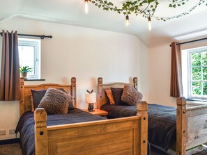 Un dormitorio con dos camas de madera, una mesita de noche, una lámpara y una ventana con cortinas.
