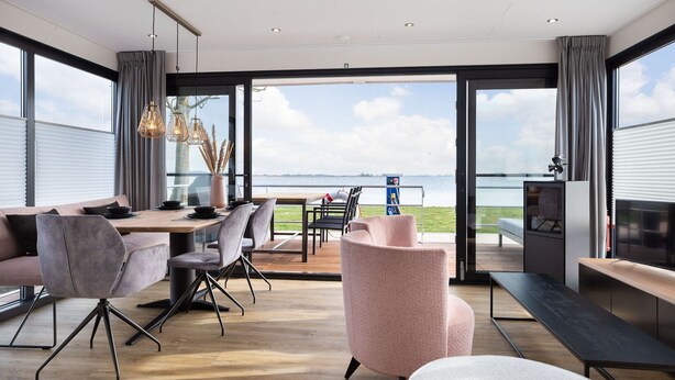 Een moderne woonkamer met een groot raam, een eethoek en een zithoek met uitzicht op zee.