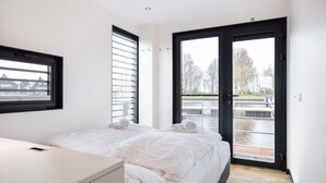 Een moderne hotelkamer met twee bedden, een groot raam en uitzicht op een gracht.