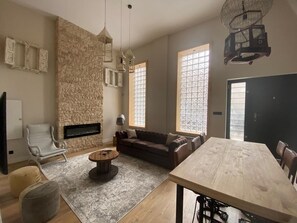 A spacious living room with a stone accent wall, a fireplace, a dining table, and large windows providing natural light. - Nice apartment in the center of Santander (Santander)