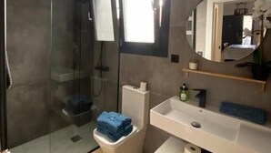 Et moderne badeværelse med et glasbrusekabine, en hvid vask og et spejl med rund ramme.
